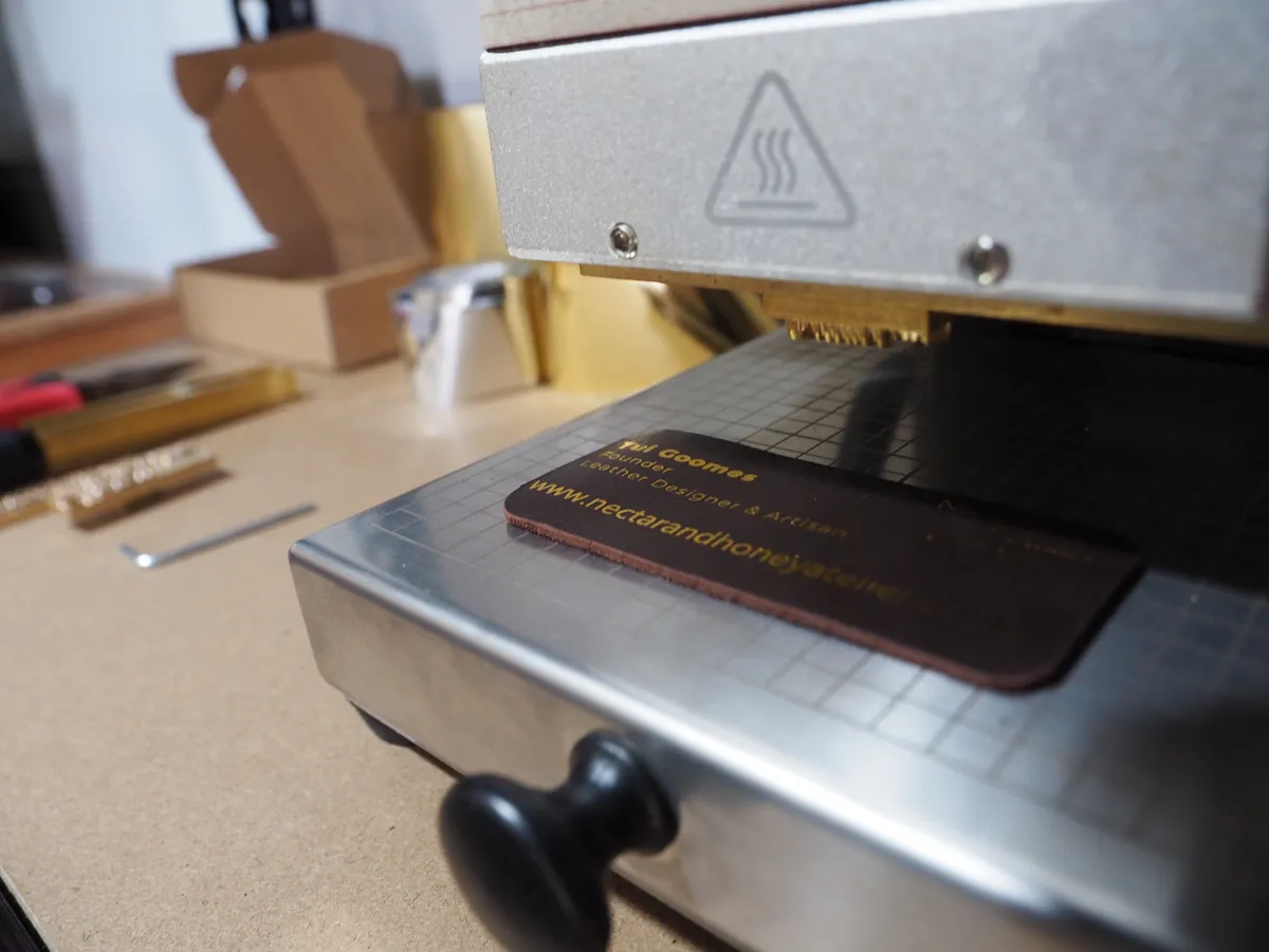 Tui hot-foil stamping the Nectar & Honey Atelier maker's mark onto a leather tag in her studio